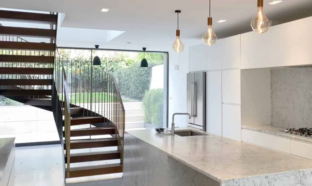 From the mezzanine level, a sculptural staircase descends into a contemporary London kitchen diner, complete with bi-fold doors that seamlessly connect the indoor and outdoor spaces.